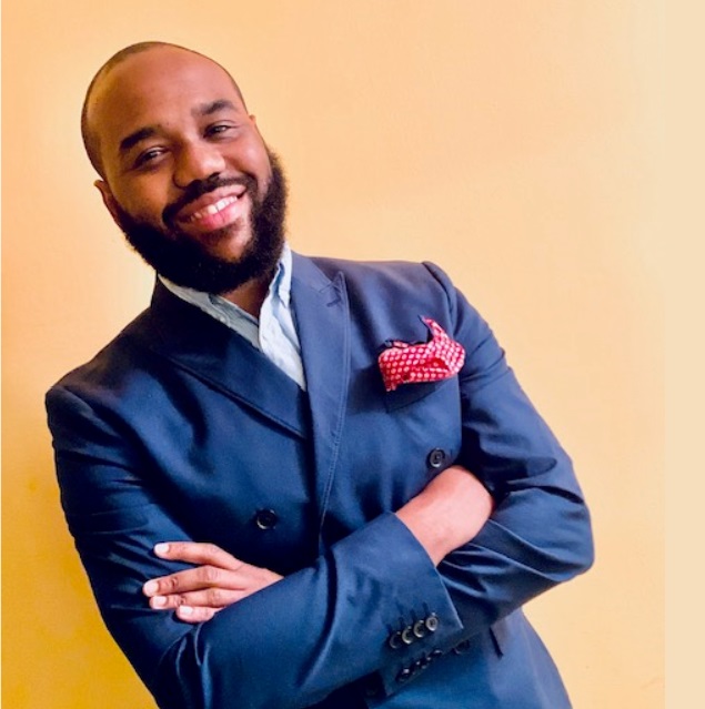 David Powel leans against a wall, smiling and with his arms corssed.