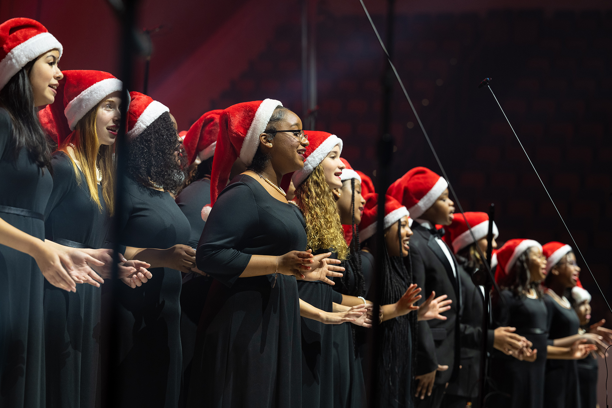 Photo of the Washington Performing Arts Children of the Gospel Choir singing on a stage, wearing red Santa hats.