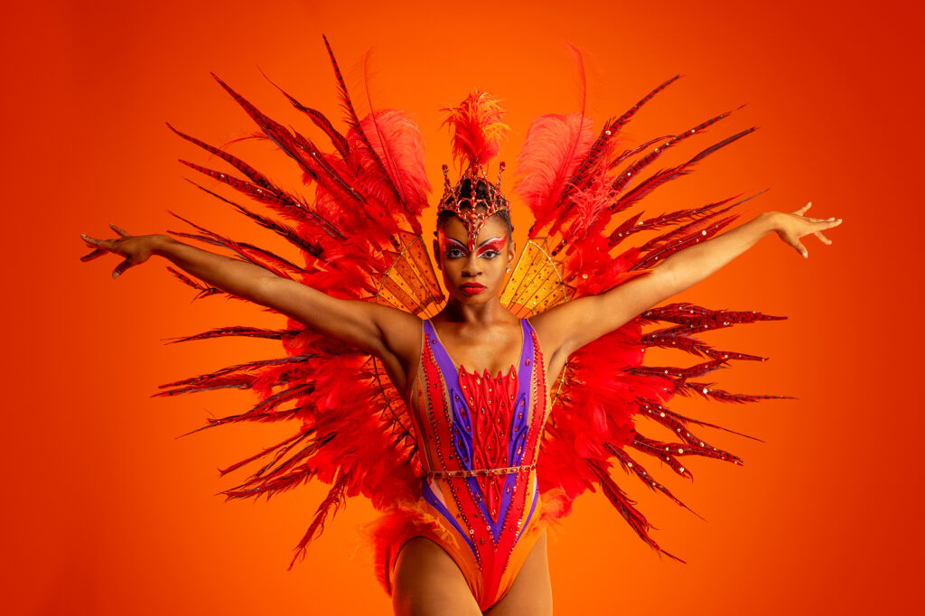A dancer in a feathery red and purple phoenix costume poses.
